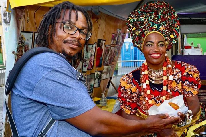 A traveler buying acarajé from a baiana in traditional dress